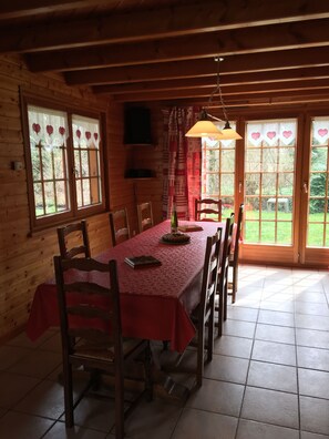 L’intérieur d’un chalet en bois comprend une table à manger, des chaises, un téléviseur et de grandes fenêtres avec des rideaux.