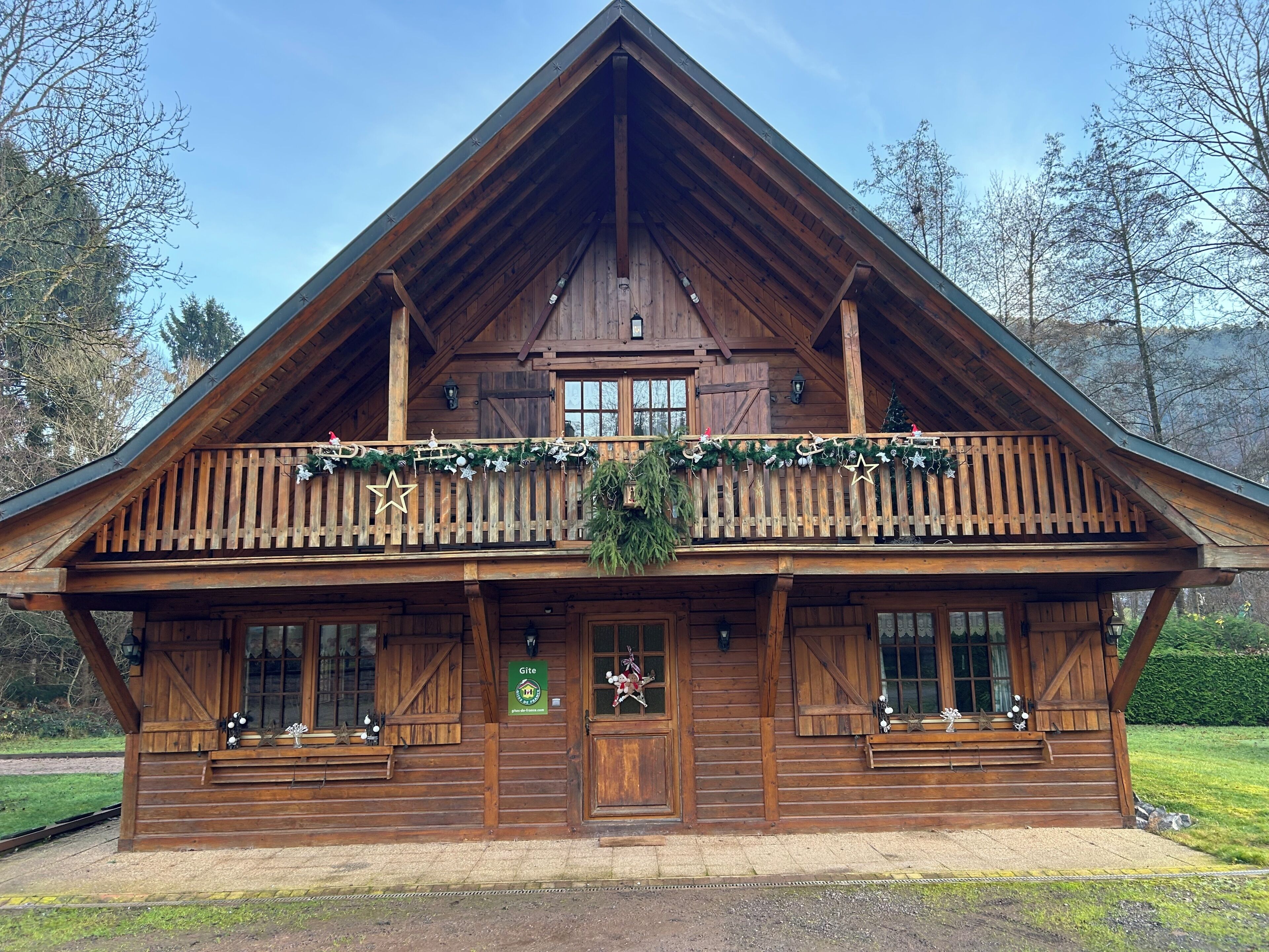A wooden cabin with a balcony, a front door, and a sign that reads 'Gite.'