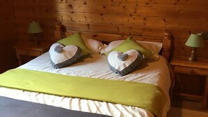 Een houten bed met een groene deken, twee hartvormige kussens en twee bedlampjes.
