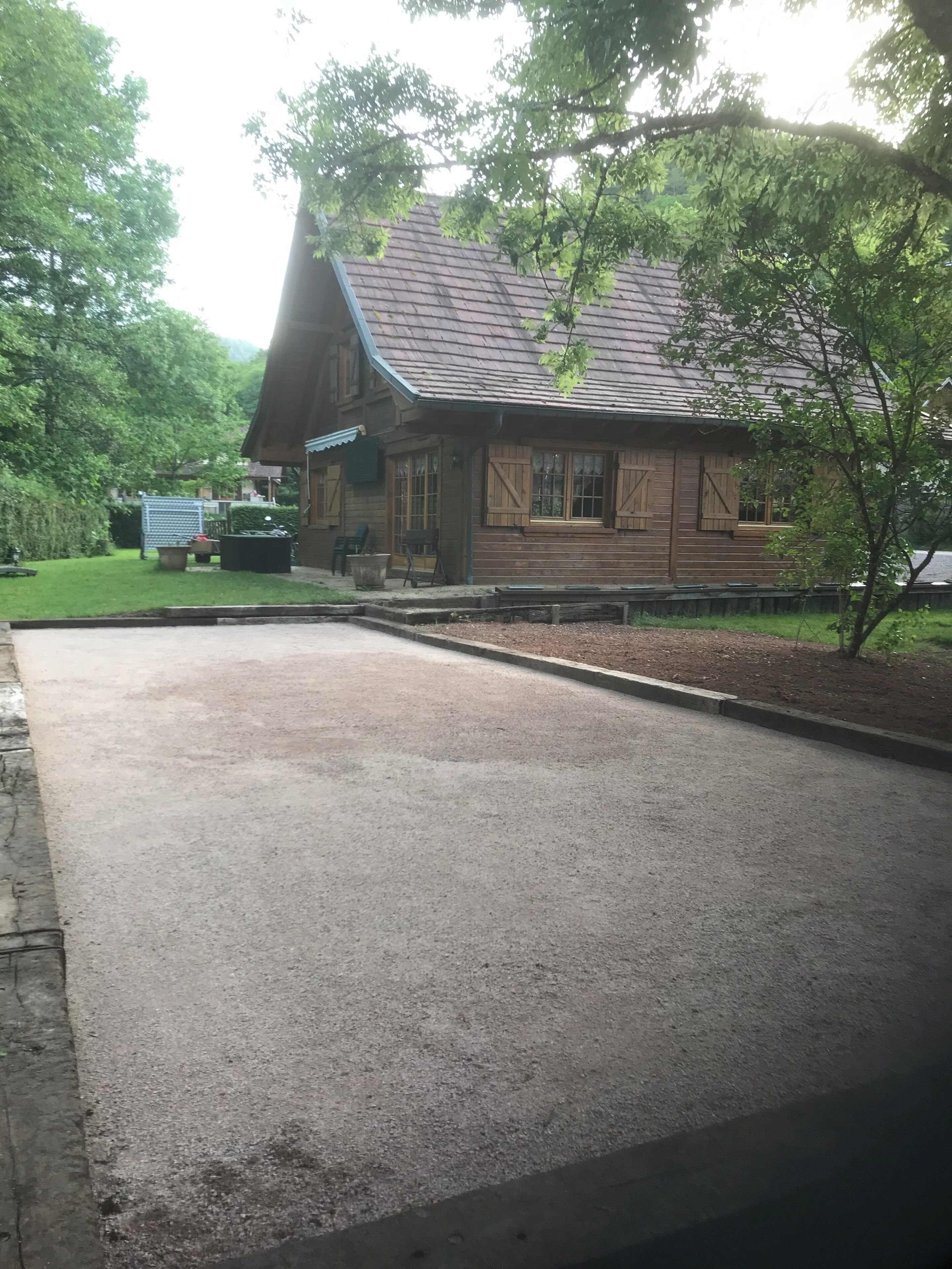 Uma cabana de madeira com telhado inclinado, um caminho de acesso pavimentado e uma área gramada com um banco.