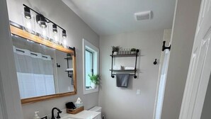 Un bagno con un mobile lavabo bianco, uno specchio, un WC e uno scaffale con articoli da toilette.