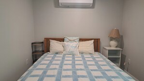 A bed with a checkered bedspread, a bedside lamp, and a wall-mounted air conditioner. - 2 Bedroom Condo Less Than A Mile To Rehoboth & Dewey Beaches (Rehoboth Beach)