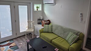 A living room with a green sofa, a white chair, a black coffee table, a ceiling fan, an air conditioning unit, a small plant, and a bookshelf. - 2 Bedroom Condo Less Than A Mile To Rehoboth & Dewey Beaches (Rehoboth Beach)