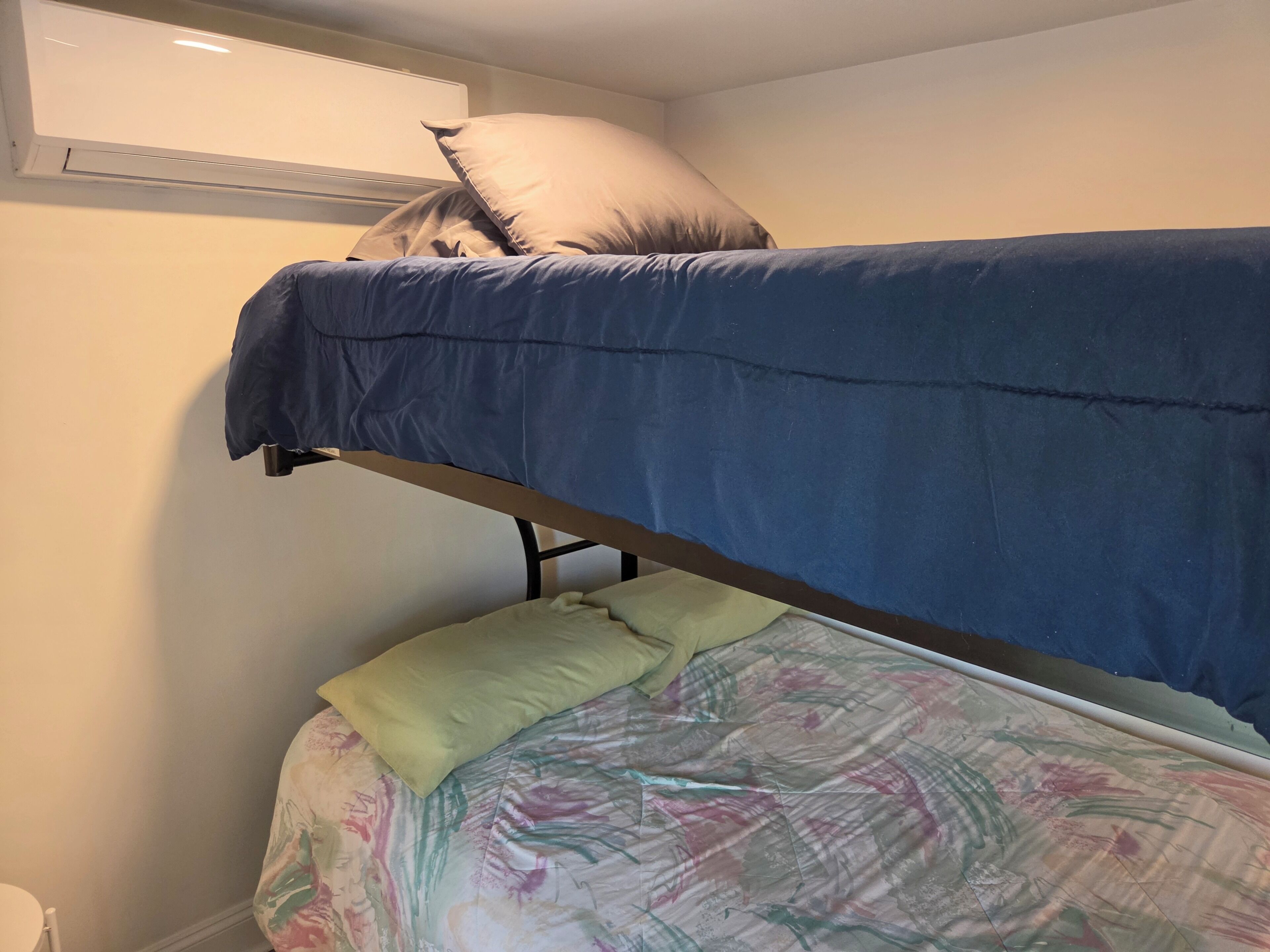 A bunk bed with a blue mattress and a lower bed with a floral-patterned sheet.