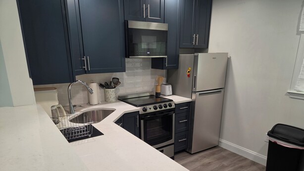 A modern kitchen with dark cabinets, a stainless steel refrigerator, a microwave, a stove, and a sink. - 2 Bedroom Condo Less Than A Mile To Rehoboth & Dewey Beaches (Rehoboth Beach)