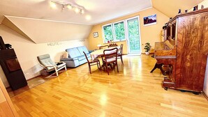 Uma sala de estar ampla com piso de madeira, uma mesa de jantar com cadeiras, um sofá e um piano.