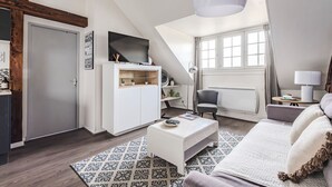 Ein Schlafzimmer im Loft-Stil mit schräg verlaufender Decke, einem großen Fenster, einem weißen Bett, einem weißen Couchtisch und einem an der Wand montierten Fernseher.
