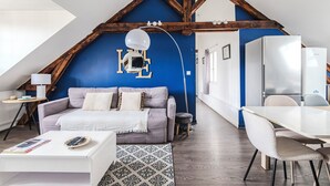 Ein gemütliches Schlafzimmer im Loft-Stil mit schrägverdeckter Decke, einem Bett, einem Schreibtisch und einem Essbereich.