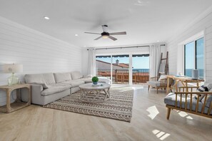 Un salon moderne avec un canapé, une table basse et des fauteuils, un balcon avec vue et un ventilateur de plafond.