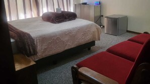 Een hotelkamer met een bed, een nachtkastje, een rode stoel, een kleine prullenbak en een wandlamp.