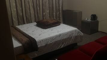 Quarto com cama, sofá vermelho, mesa de cabeceira de madeira, controle remoto, aquecedor e TV fixada na parede.