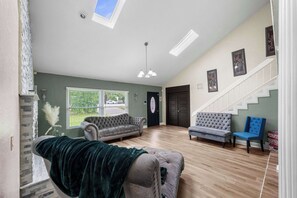 Ein großzügiges Wohnzimmer mit hoher Decke, einer Treppe und Blick ins Freie.