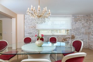 Ein Esszimmer mit Glastisch, roten Stühlen, einer Kristallleuchtre und einer Steinwand.