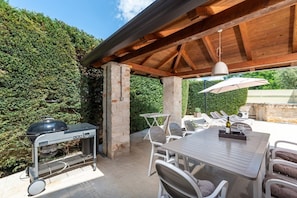 Eine Terrasse im Freien mit Grill, Esstisch, Stühlen und einer hängenden Leuchte.