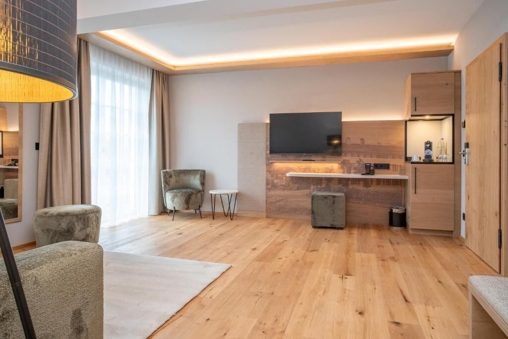 Ein modernes Wohnzimmer mit einem Flachbildfernseher, einer Couch, einem Sessel, einem kleinen Tisch und einer Küchenzeile mit Arbeitsfläche und Schränken.