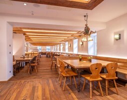 Un amplio comedor con mesas y sillas de madera, techo alto con vigas a la vista e iluminación colgante.