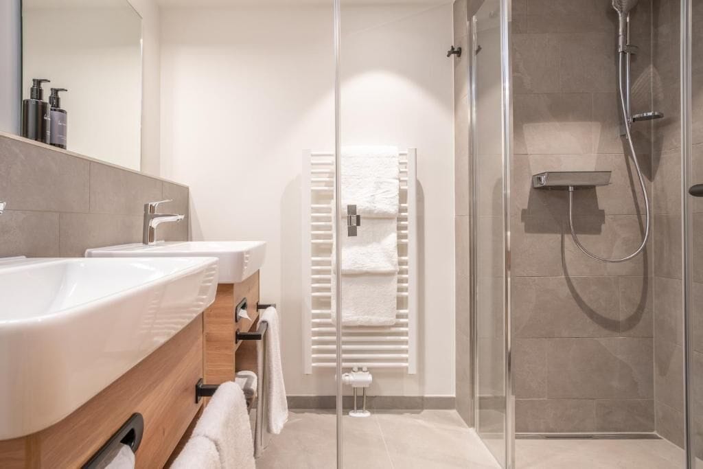 A modern bathroom with a glass shower enclosure, a white sink, and a towel rack.