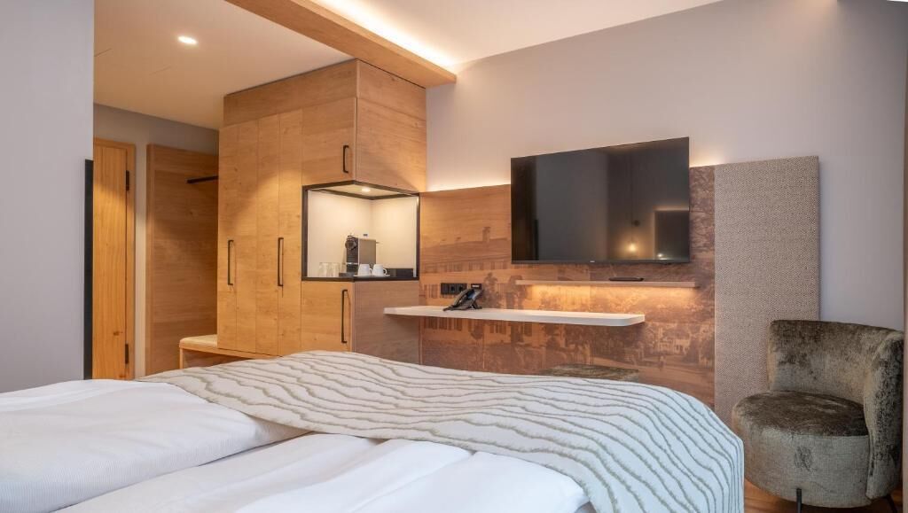 Un dormitorio moderno con una cama, un armario de madera, un televisor montado y una silla.