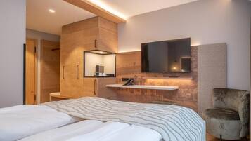Un dormitorio moderno con una cama, un armario de madera, un televisor montado y una silla.