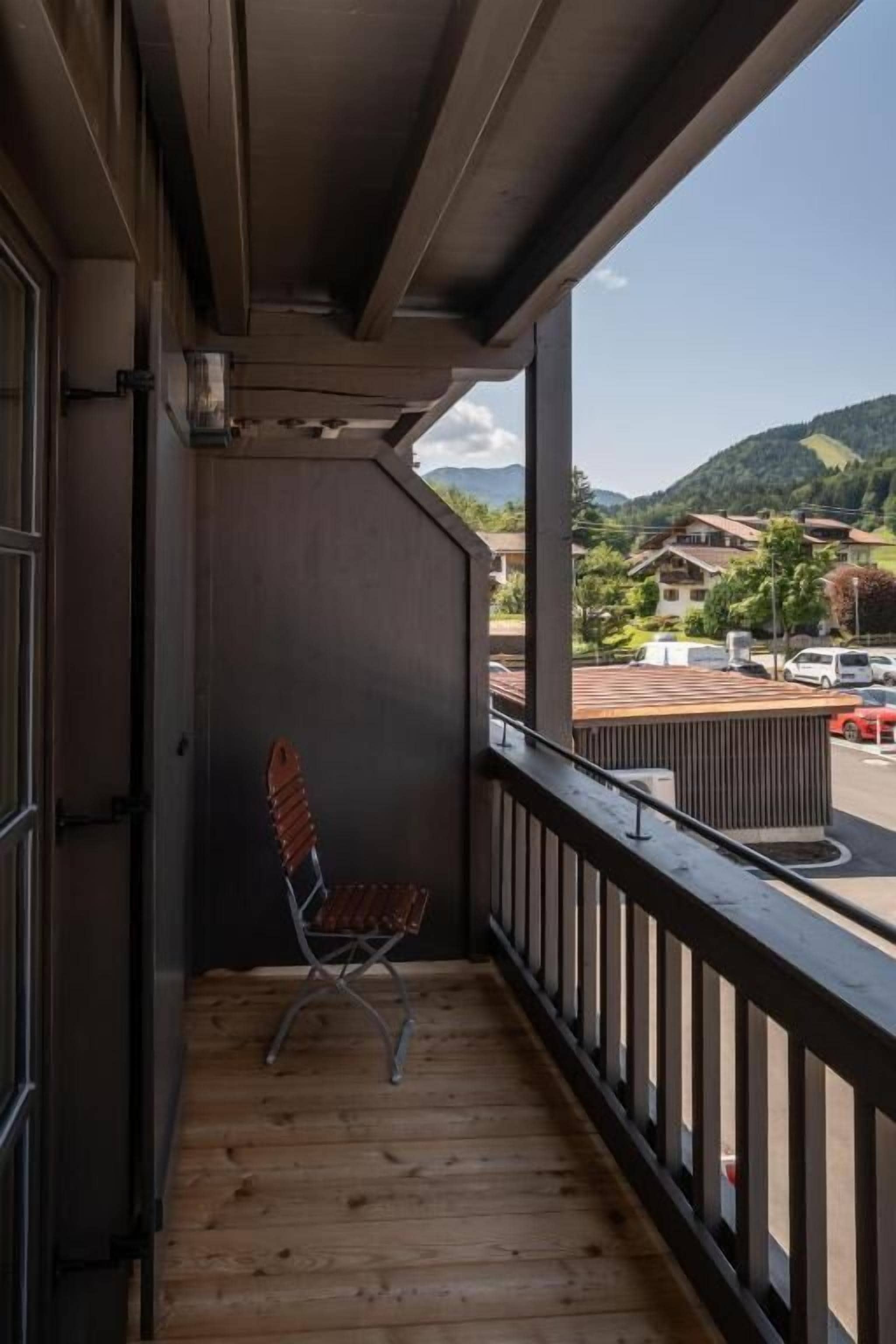 En balkon med trægulv, en metalstol og udsigt til en gade og bakker.