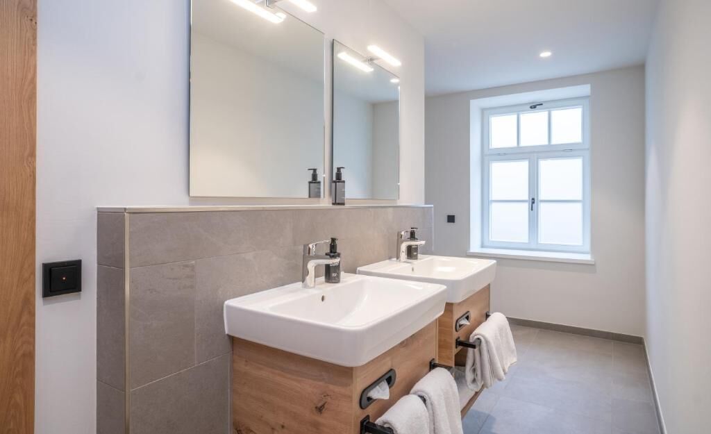 Un baño moderno con dos lavamanos, un espejo grande y una ventana.