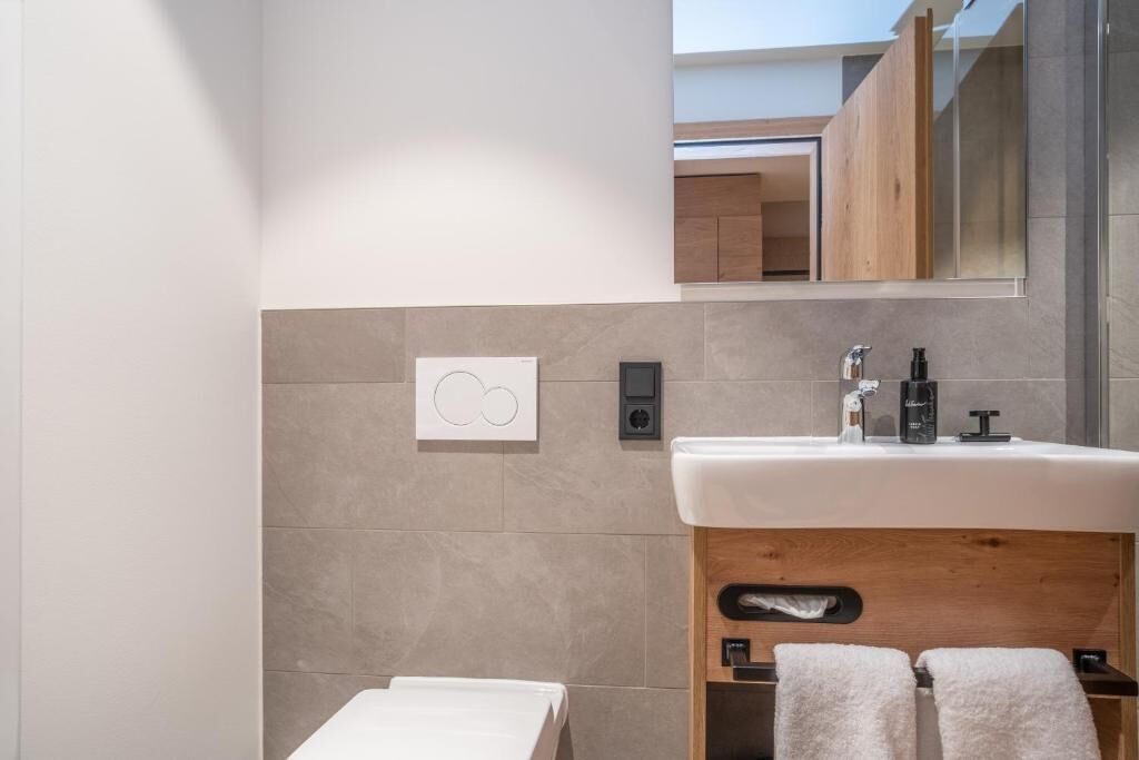 Ein modernes Badezimmer mit einem weißen Waschbecken, einem Holzkästen und einem Handtuchhalter.