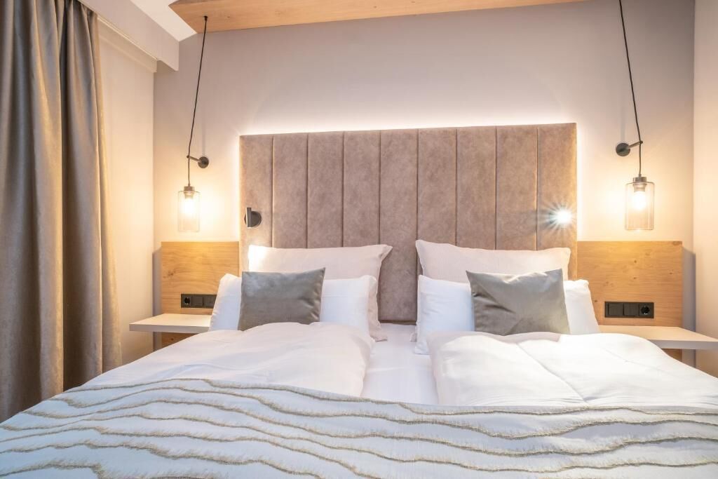 A modern hotel room with a large bed, wooden headboard, bedside tables, and pendant lighting.