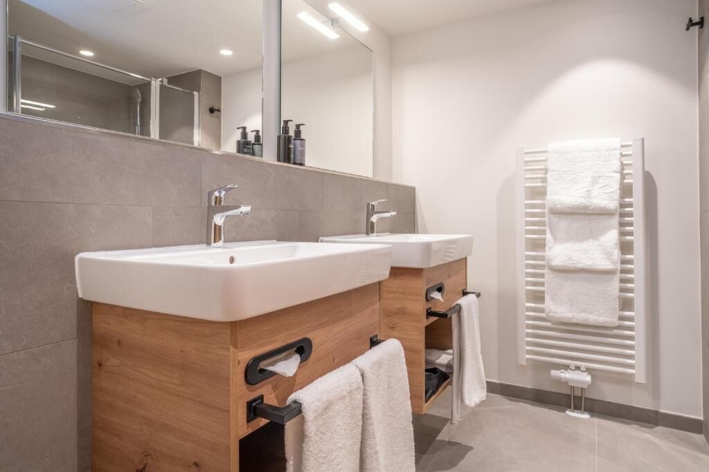 A modern bathroom with two sinks, a mirror, and a towel rack.
