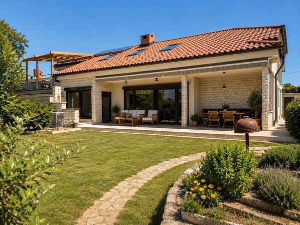 Ein modernes Haus mit überdachter Terrasse, Rasen und einem Blumenbeet.