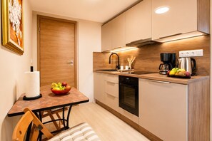 Eine kompakte Küche mit Holztischplatte, integriertem Backofen, Kaffeemaschine und Obstschale auf dem Tisch.