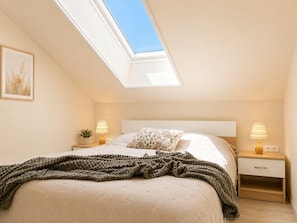 Ein Schlafzimmer mit Dachfenster, einem Bett mit gemustertem Kissen, zwei Nachttischlampen und einem kleinen Nachttisch.