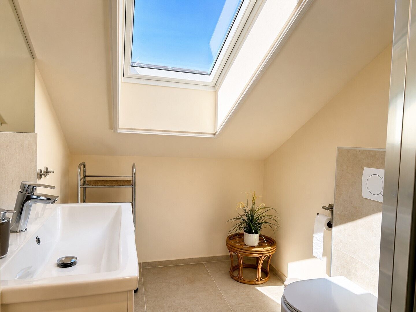 Ein kleines Badezimmer mit Dachfenster, Waschbecken, Toilette und einem runden Tisch mit Pflanze.