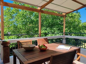 Ein Holztisch mit Stühlen, einer Schüssel und einer Obstschale auf einem Balkon mit Blick auf grüne Bäume.