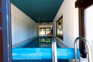 Ein Hallenbad mit freiem Blick auf den Poolbereich, ein Fenster mit Aussicht ins Freie und eine Tür zu einem anderen Raum.