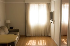 A room with a sofa, a TV on a stand, and a window with curtains. - Apartment in Jardins with parking space and pool. (São Paulo)