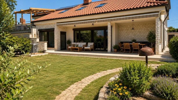 Ein modernes Haus mit überdachter Terrasse, Rasen und einem Blumenbeet.