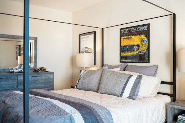 A hotel room with a bed, a nightstand, a lamp, a dresser, a mirror, and a poster on the wall.