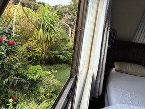A bedroom with a bed, curtains, and a window overlooking a lush garden with various plants and a small pond. - A Piece of Paradise With Your own Entrance! (Auckland)