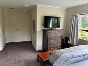 A bedroom with a bed, a dresser, a television, a window with curtains, and a door. - A Piece of Paradise With Your own Entrance! (Auckland)