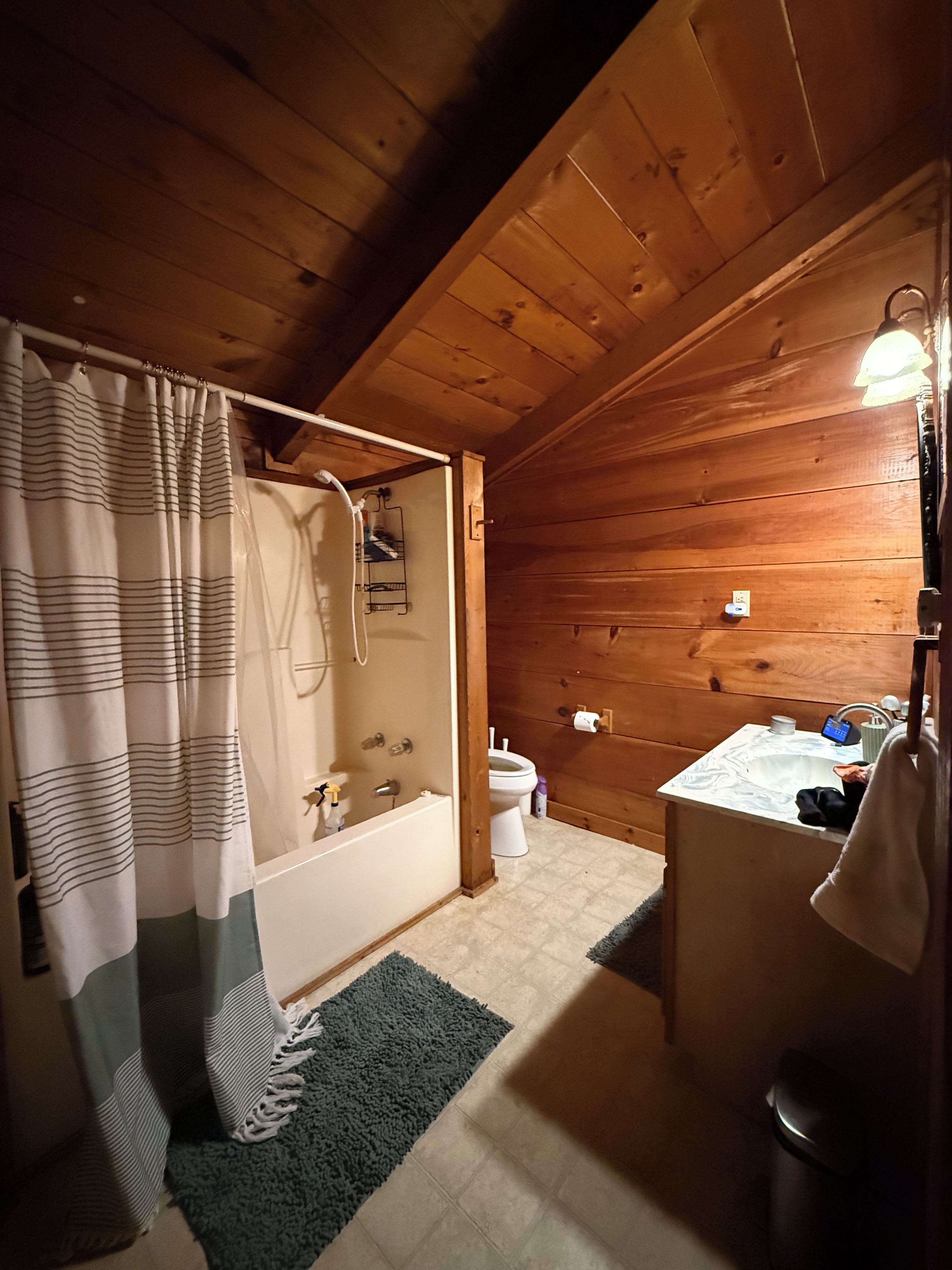 Een houten badkamertje in een vakantiehuisje, met een bad, toilet en wastafel.