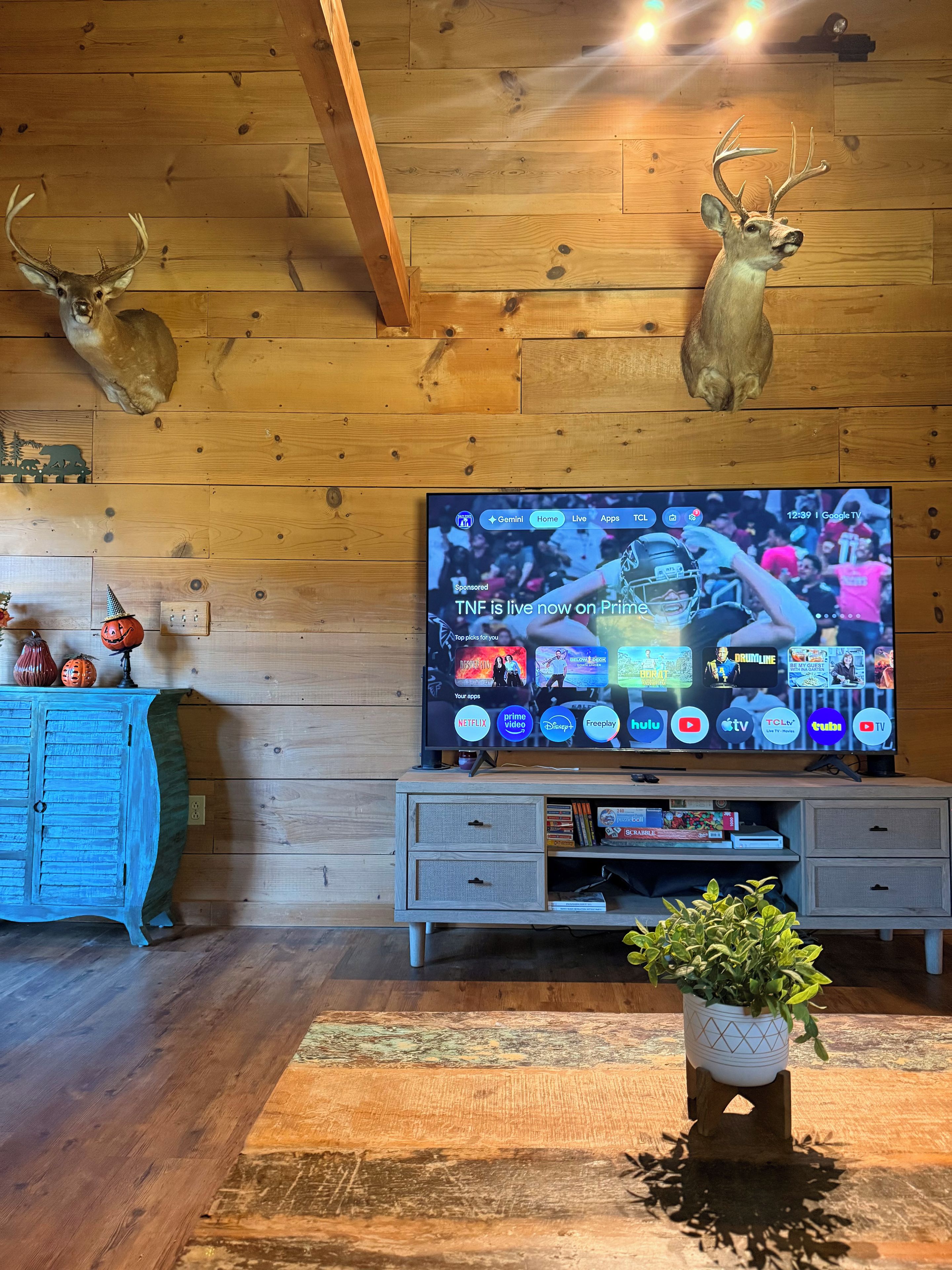 Een kamer met houten lambrisering, een televisie waarop een sportevenement te zien is, een decoratieve hertenkop en een blauwe kast.