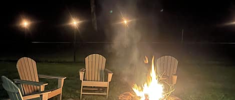 Ein Außenbereich bei Nacht mit einem Feuerkorb und zwei Adirondack-Stühlen.