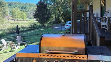 A barbecue grill on an outdoor deck with a view of a wooded area.