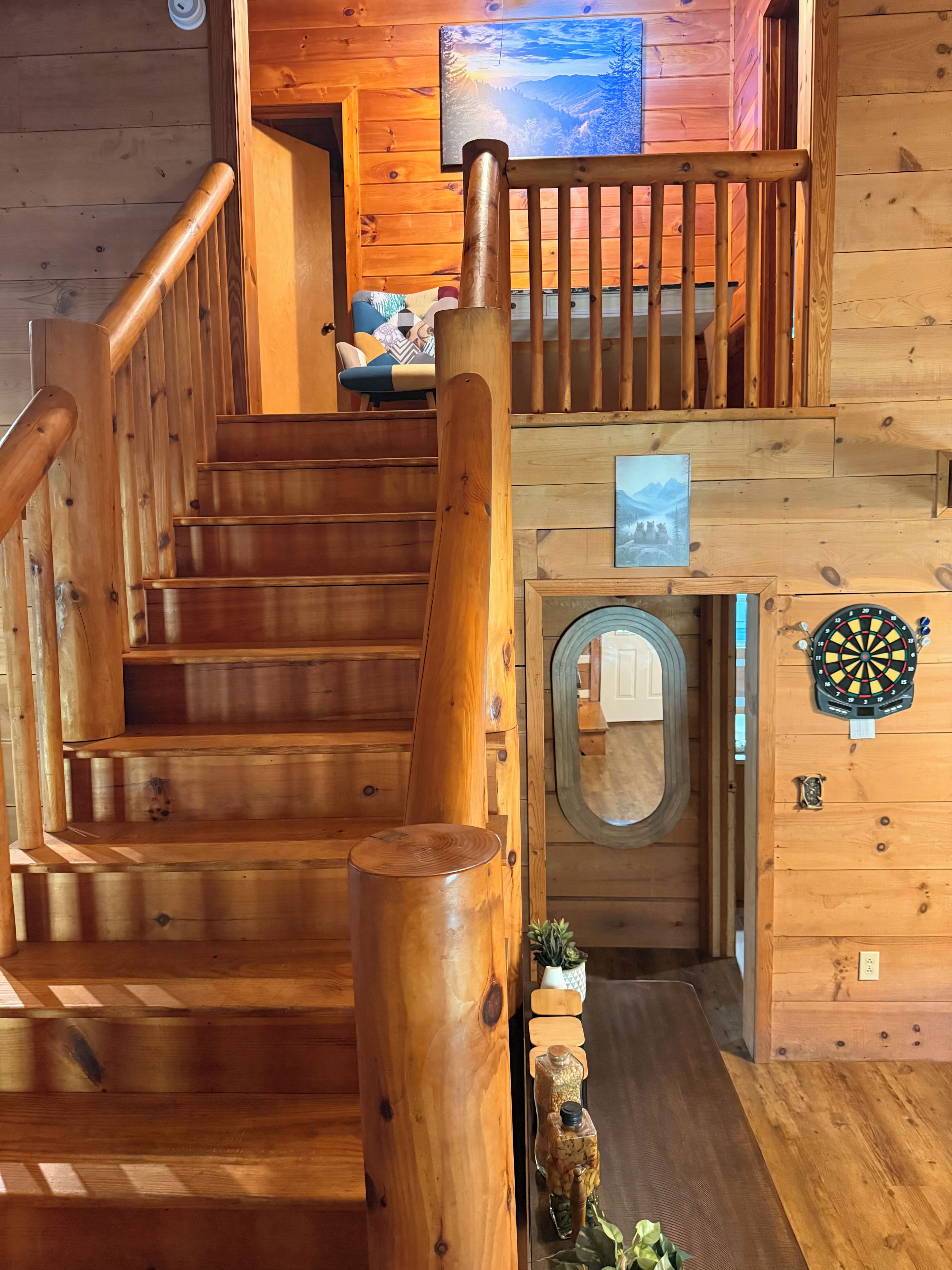 A wooden staircase with a handrail, a door with a circular window, and a dartboard on the wall.