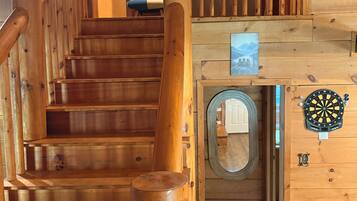 A wooden staircase with a handrail, a door with a circular window, and a dartboard on the wall.