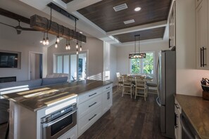 A modern kitchen with a central island, stainless steel appliances, and a dining area with wooden chairs. - Coastal Retreat with Private Pool in Historic Saint Augustine Florida (St. Augustine)