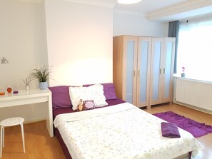 A bedroom with a bed, a desk, a wardrobe, a window with curtains, and a radiator. - Stylish, Spacious  4‑Bedroom House Near London • Ideal for Groups & Contractors (Potters Bar)