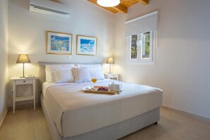 A bedroom with a bed, two bedside tables, a window, and two framed pictures on the wall. - Villa Avlaki (Vlikhon)