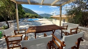 Un espacio de estar al aire libre techado, con mesa y sillas de madera, con vista a una piscina y un paisaje montañoso.