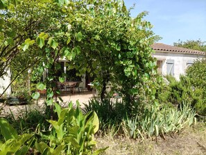 A rustic house with a garden, a dining area with outdoor furniture, and a variety of plants.